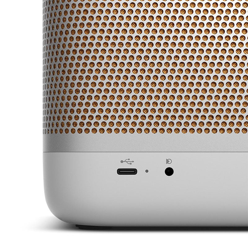 This image is a close-up of the **Bang & Olufsen (B&O) portable speaker**. It highlights the **USB-C port** and what appears to be an **audio jack** or possibly a charging indicator. The **golden-honeycomb grille** pattern is prominently featured, showing the fine detailing of the speaker's design. The bottom half of the speaker is in a sleek, **matte light grey** finish, complementing the overall premium look. The USB-C port is for charging or connectivity, emphasizing the modern design features typical of