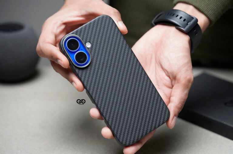 This image shows a carbon fiber-textured phone case with a sleek, modern design. The case is designed for a smartphone with a dual-camera setup, accented by a vibrant blue ring around each camera lens, adding a touch of contrast to the black carbon fiber finish. The person holding the phone case demonstrates its ergonomic design, with smooth edges that likely enhance grip and comfort. This case appears to provide a blend of style and protection, suitable for those who prefer a minimalist yet durable accesso