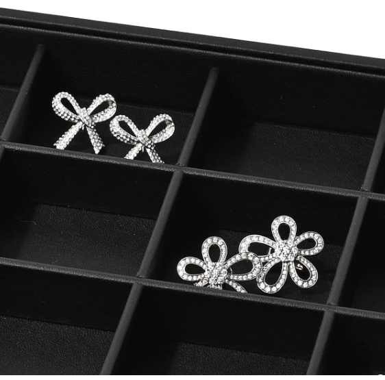 Two pairs of rhinestone earrings displayed in a black jewelry organizer tray, featuring one set with elegant bow-shaped designs and another with floral shapes.