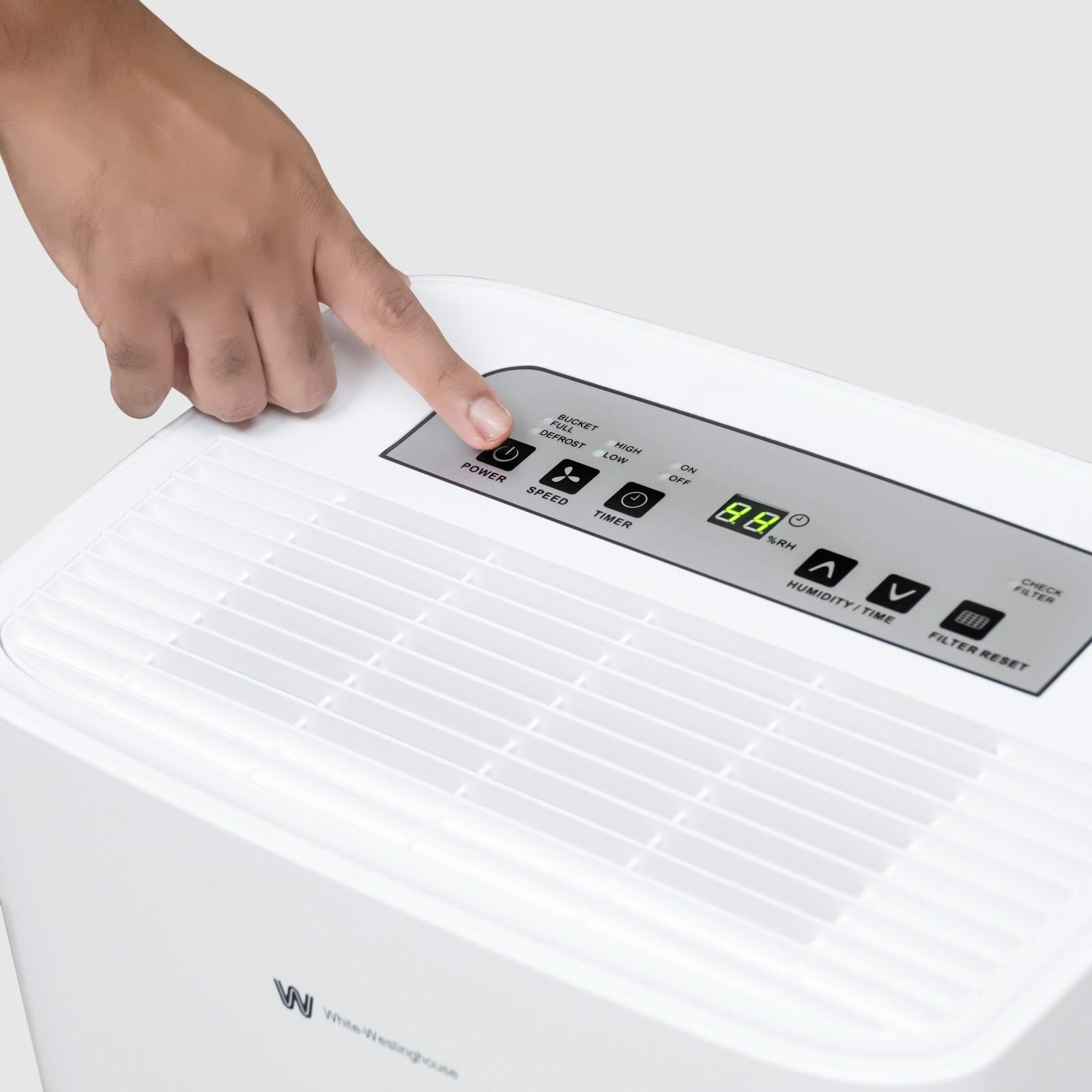 Close-up view of a user pressing the power button on the control panel of the White Westinghouse Dehumidifier AWHD306L, displaying its intuitive interface and operational settings.