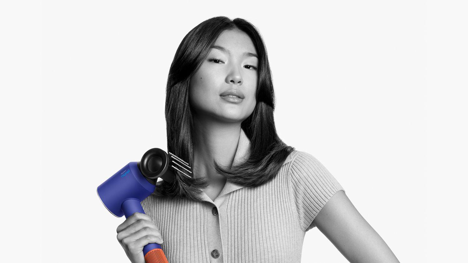 A woman with flowing hair confidently using a blue hair dryer with an orange grip, styled to highlight the product's performance.