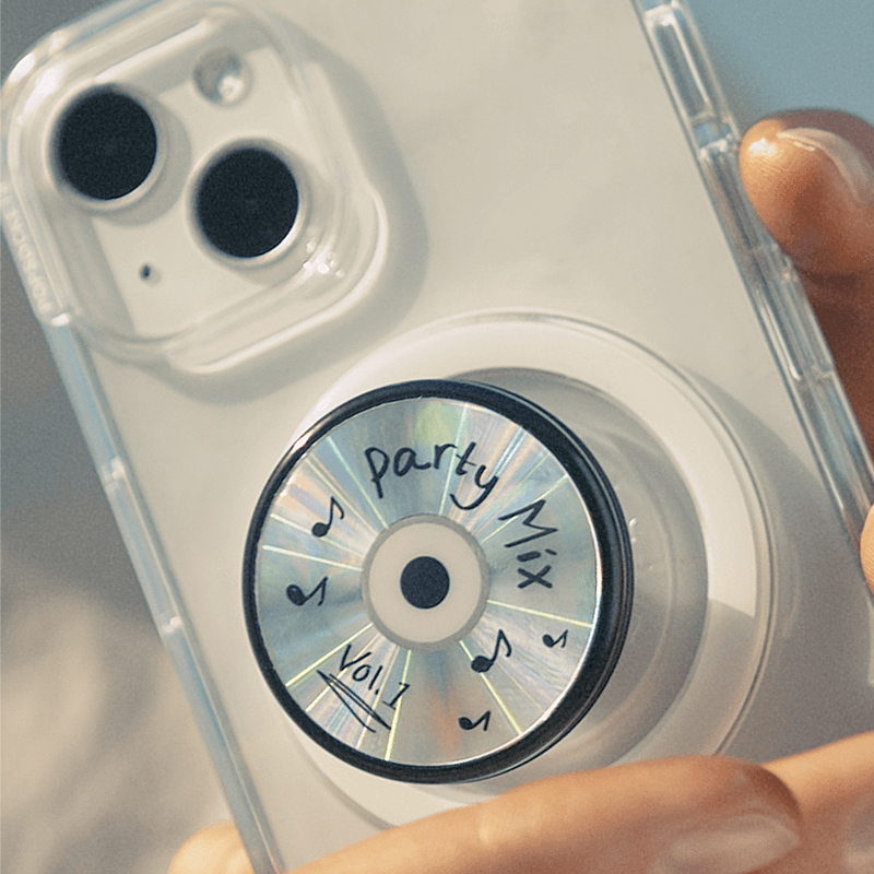 Close-up view of a hand holding a smartphone with a clear case and a PopSockets PopGrip Backspin attached to the back. The PopGrip features a design of a CD labeled "Party Mix Vol. 1" with a shiny, iridescent surface and handwritten-style text and musical notes around the label. The phone and PopGrip are shown in natural light, highlighting the holographic effect of the CD design.