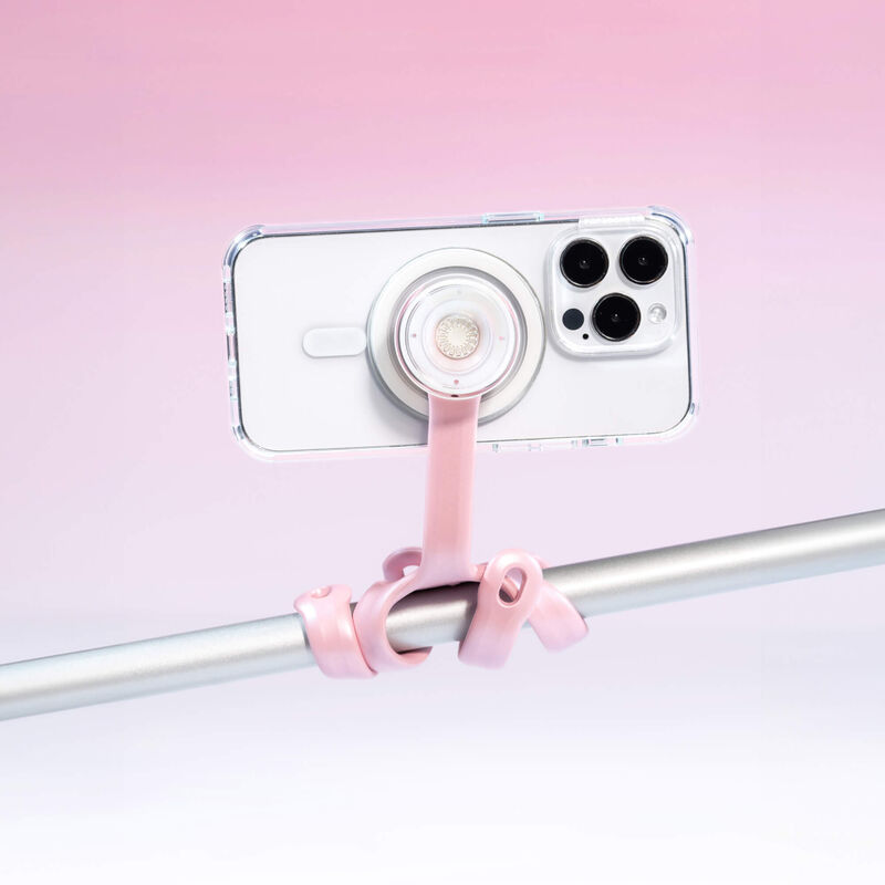 PopSockets Flex Mount in Pinky color holding a smartphone in a clear case with a white PopGrip attached to the back. The mount's flexible legs are wrapped around a horizontal metal bar, securing the smartphone in a horizontal position. The phone is shown from the back, highlighting the PopGrip and the light pink colored flexible mount's secure attachment. The setup is displayed against a light pink background