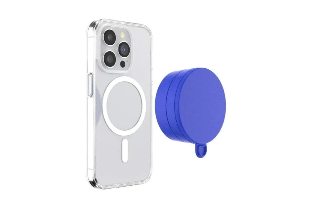  A smartphone with a clear case is shown next to a cobalt blue PopSockets Suction Mount for MagSafe. The phone's back features the MagSafe alignment ring, indicating compatibility with MagSafe accessories. The mount is positioned beside the phone, showcasing its vibrant color and circular design. The clear case allows the MagSafe ring and the phone's details to be visible, emphasizing the mount's functional and stylish design.