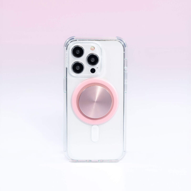 A smartphone with a clear case is shown with a PopSockets MagSafe PopGrip in dusty rose color attached to its back. The PopGrip features a glossy, slightly reflective soft pink surface, positioned centrally on the phone's back. The phone's camera lenses are visible at the top, highlighting the PopGrip's sleek and modern design, which complements the phone's aesthetics while providing a functional grip