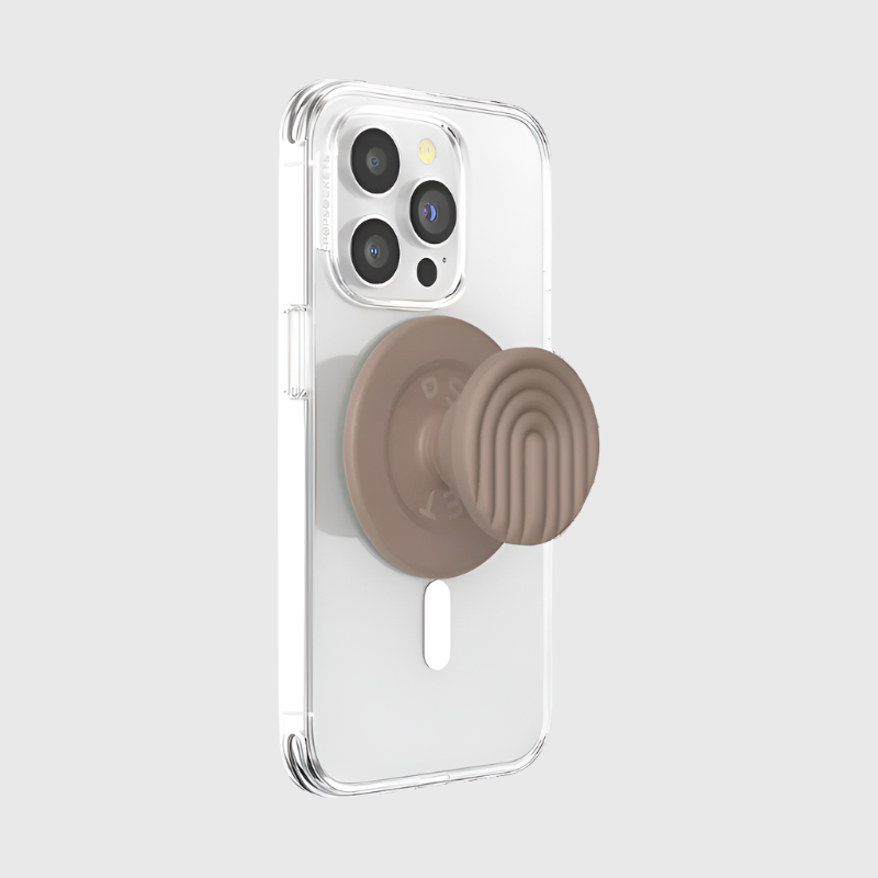  A clear phone case is shown attached to a smartphone with a PopOut Latte Curves PopGrip for MagSafe. The PopGrip, featuring a latte-colored design with curved lines, is fully extended, providing a secure and stylish hold for the device