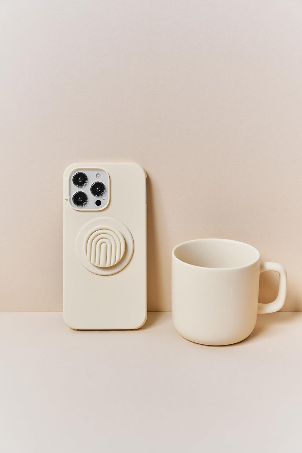 This image displays a beige-toned aesthetic featuring a smartphone with a pale yellow case and matching PopSocket alongside a similarly colored ceramic mug. The PopSocket, attached to the phone case, has a raised arch design for a modern and minimalist appearance. The cohesive color scheme creates a soft, neutral, and calming vibe, perfect for a stylish and functional setup. The ceramic mug complements the phone's look, tying the scene together with a clean and minimalist aesthetic.