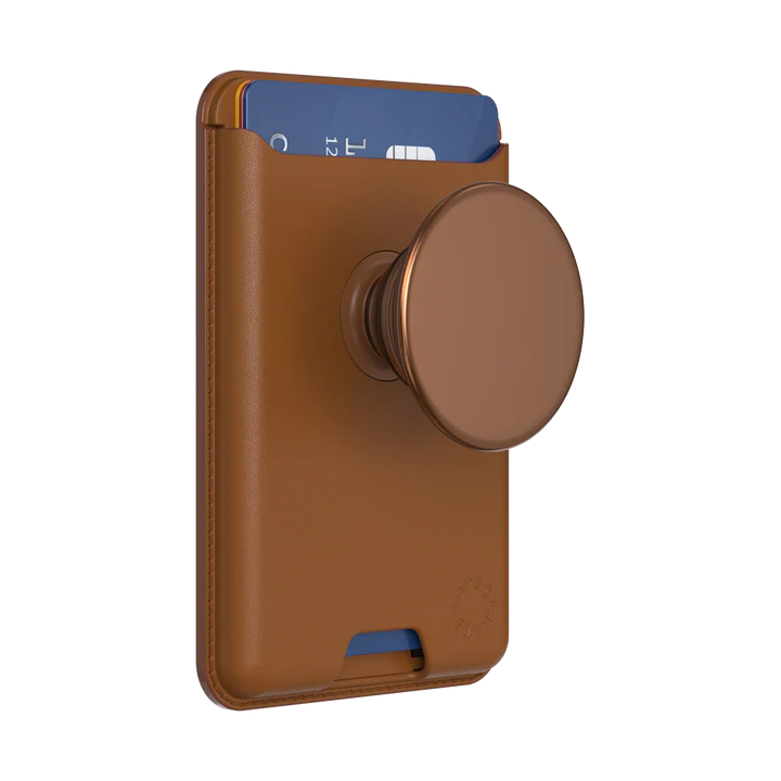 PopSockets MagSafe Softgoods PopWallet in Cognac. The wallet, designed for holding cards, is attached to a circular PopSocket of the same cognac color. The wallet is shown with a card partially inserted, showcasing its functionality. The PopSockets logo is embossed near the bottom right corner. The material appears to be a soft, leather-like texture with clean stitching along the edges.