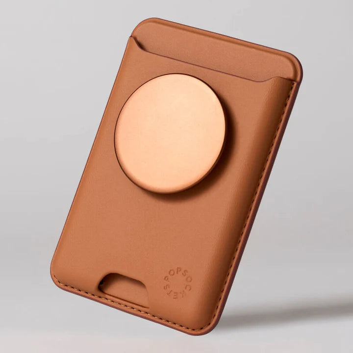 A PopSockets MagSafe Softgoods PopWallet in Cognac, shown from the back. The wallet features a cognac-colored circular PopSocket in the center. The material appears to be leather or a leather-like texture, with visible stitching along the edges. The PopSockets logo is embossed near the bottom right corner of the wallet.