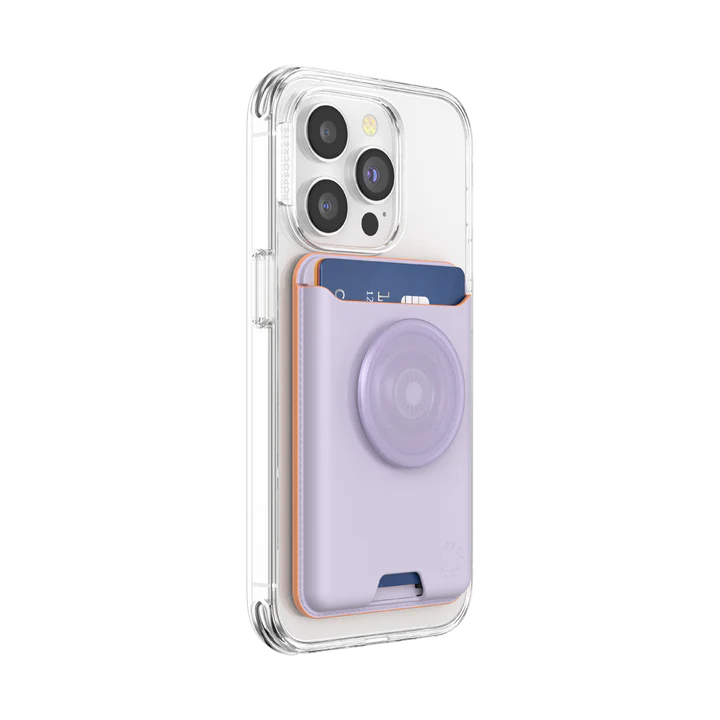  A clear-cased iPhone with a PopSockets MagSafe Softgoods PopWallet in Pale Lavender attached to the back. The wallet holds a blue credit card and features a circular PopSocket in the same lavender color. The PopSockets logo is embossed near the bottom right corner of the wallet. The phone and wallet are positioned at an angle, showing the thickness and fit of the wallet on the phone.