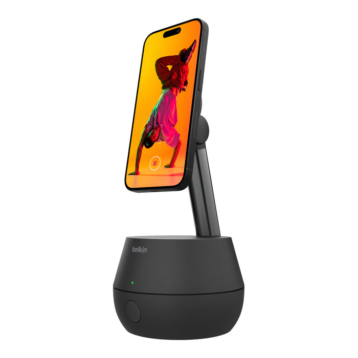 A sleek black Belkin charging stand holding a smartphone upright. The phone screen displays a colorful image of a person in a yoga pose against a vibrant orange background. The stand features a minimalistic design with a small green LED indicator.