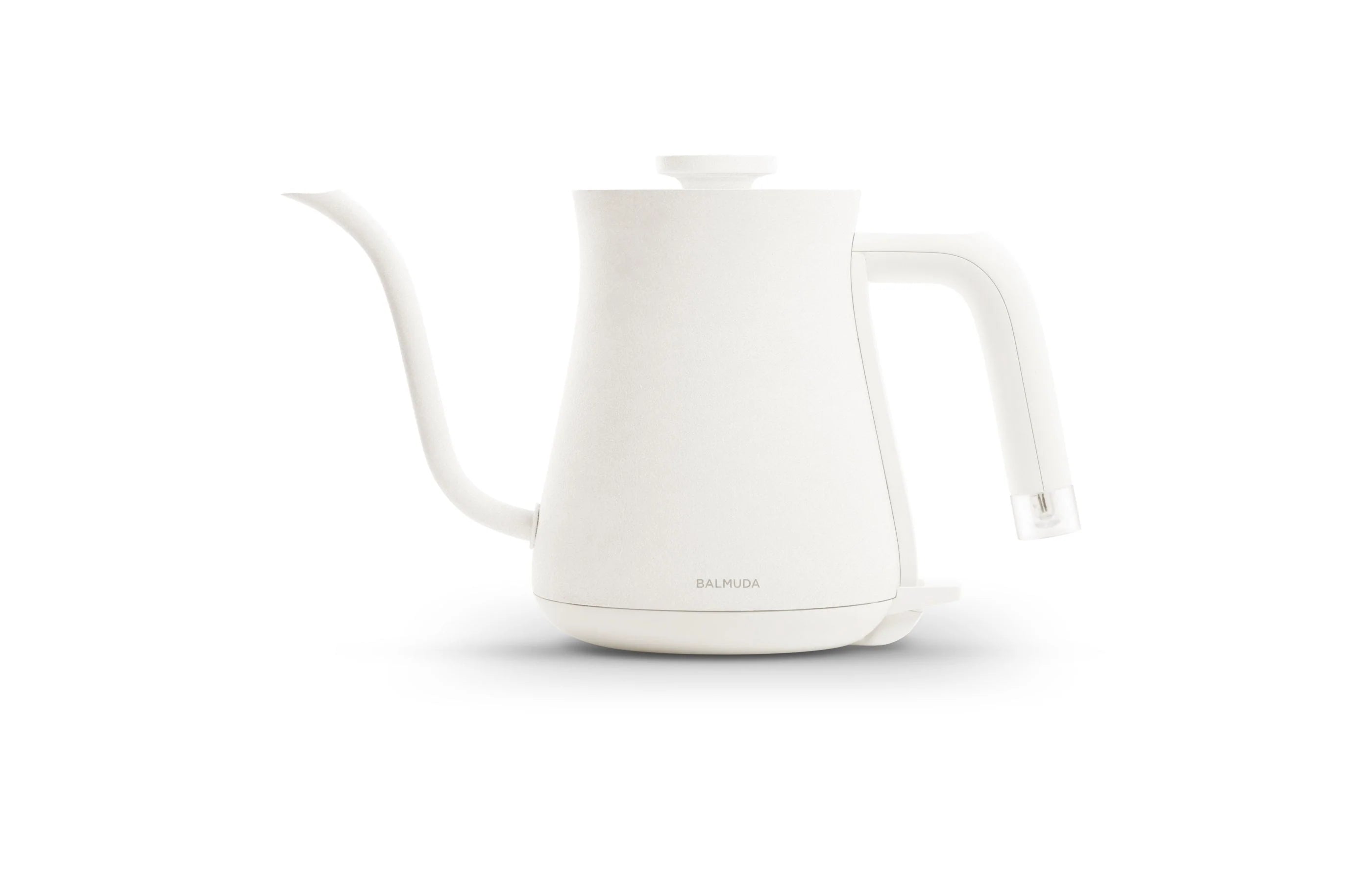 The image shows a Balmuda electric kettle in a clean, matte white finish against a plain white background. The kettle features a minimalist and modern design with a long, curved spout for precise pouring and a straight, ergonomic handle with a clear accent at the base. The brand name "BALMUDA" is subtly printed near the bottom of the kettle’s body. The design emphasizes simplicity, elegance, and functionality, making it a stylish and practical appliance for any kitchen.