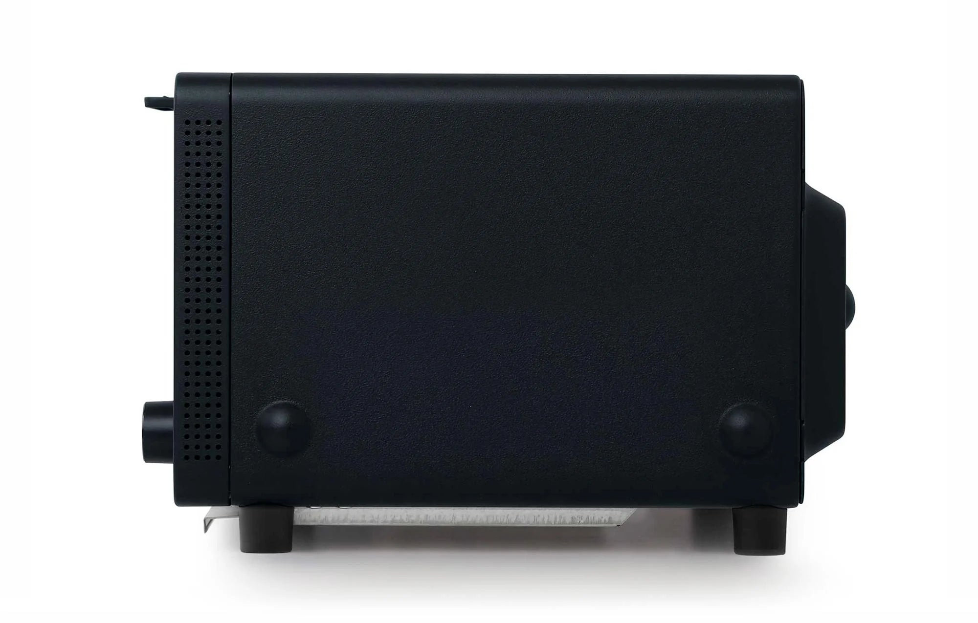  The image shows a side view of a Balmuda toaster in a matte black finish. The side panel is smooth and minimalist, with two small circular feet near the bottom for stability. Toward the front, there is a series of small ventilation holes arranged in a vertical line, providing airflow to the interior components