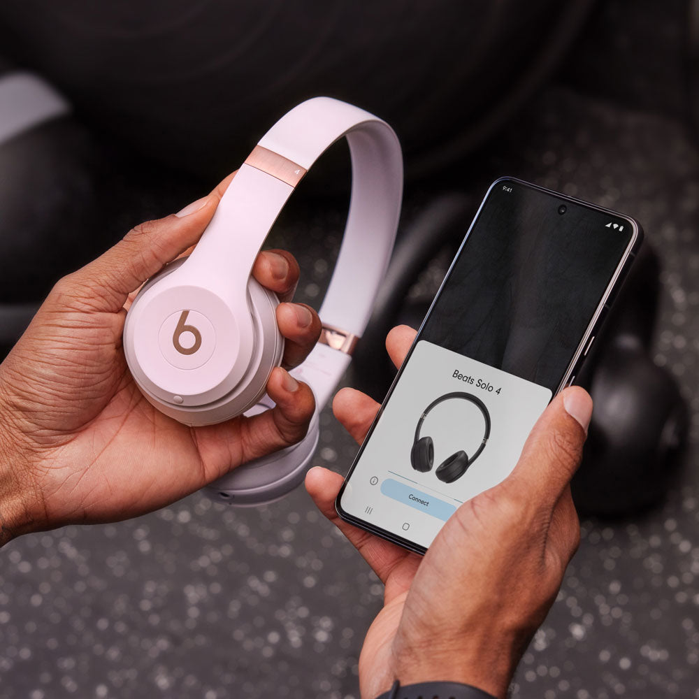 "Hands holding pastel purple Beats by Dre headphones while connecting to a smartphone, highlighting wireless connectivity and modern design."