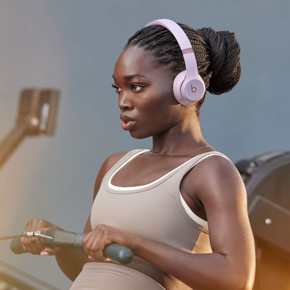 A woman exercising while wearing Beats Solo 4 wireless headphones in pink, highlighting the headphones' stylish design and comfortable fit for active use.