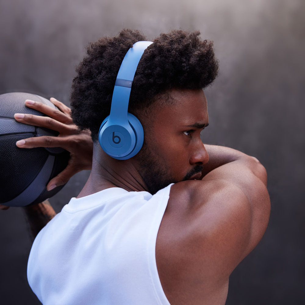 "Man wearing blue Beats by Dre wireless over-ear headphones while holding a basketball, emphasizing athletic style and high-performance audio."