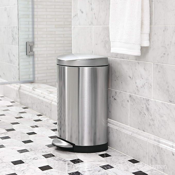 A sleek and modern stainless steel trash bin placed in a stylish bathroom with marble tiles, featuring a foot pedal for convenient hands-free operation.