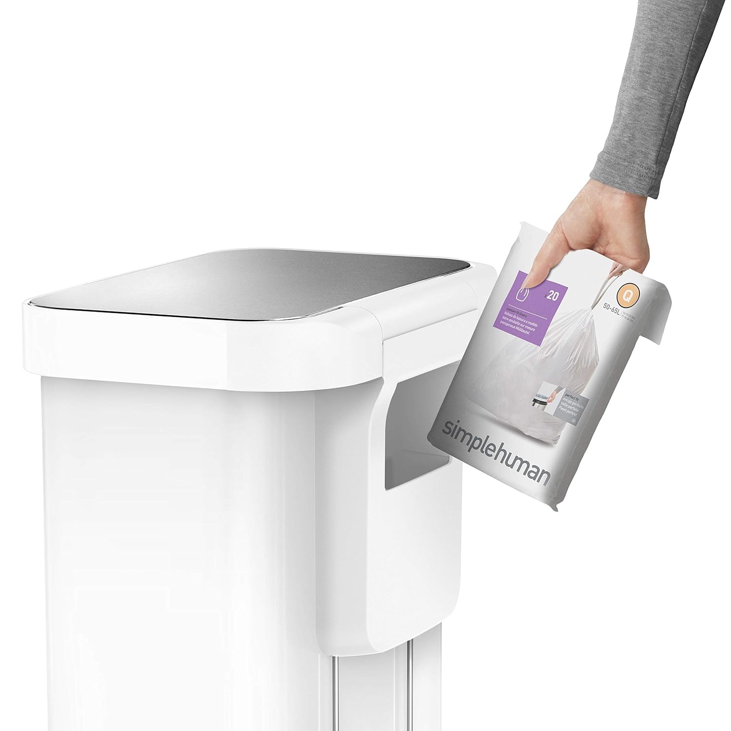 A close-up image showing a person inserting a Simplehuman trash bag refill pack into a built-in storage pocket on a sleek, white Simplehuman trash bin. The trash bin features a stainless steel lid, adding a modern and sophisticated touch, and the design emphasizes convenient access to the liners for easy replacement.