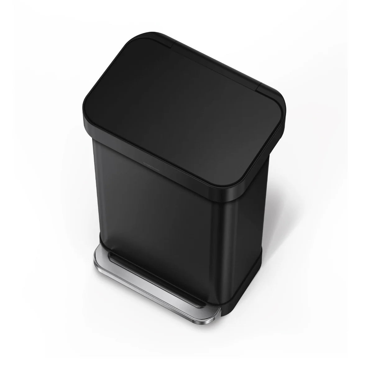 The image shows a top-down view of a black Simplehuman trash can with a closed lid. The trash can has a rectangular shape with rounded edges and a sleek, matte black finish. The foot pedal at the base is visible, with a metallic finish that contrasts with the black body of the can. The design is modern and minimalist, emphasizing both form and function. This perspective highlights the trash can's compact footprint and clean lines, making it a stylish and practical addition to any space.