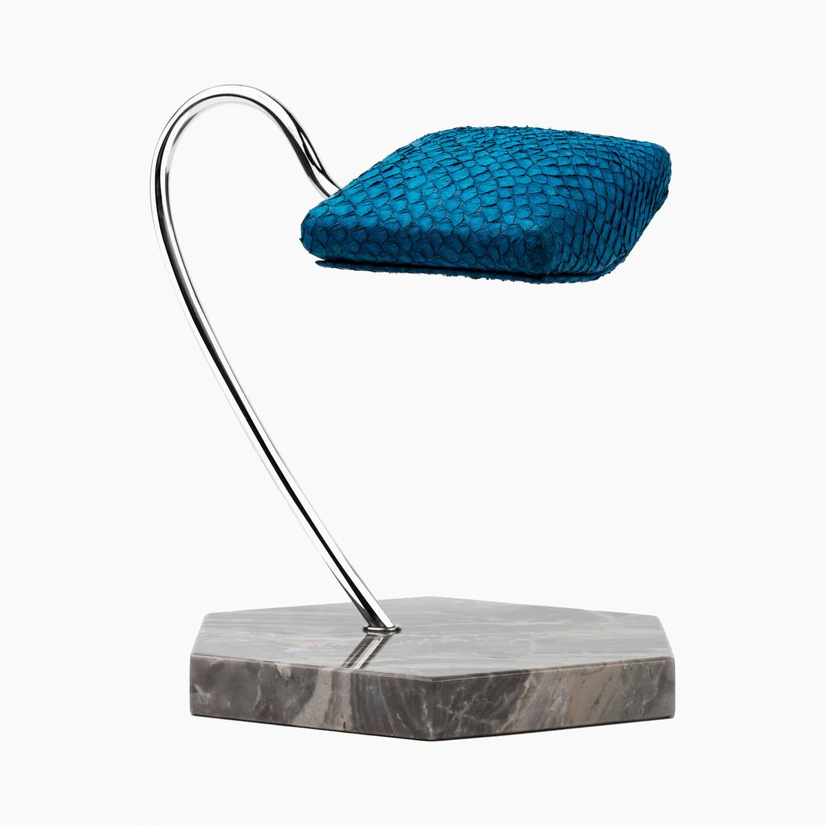 An elegant display stand featuring a blue textured cushion mounted on a sleek, curved metal support. The base of the stand is a hexagonal marble slab with shades of gray and brown veining. The design is modern and sophisticated, ideal for showcasing a wristwatch or similar item. The vibrant blue cushion contrasts beautifully with the polished metal support and marble base, creating a luxurious presentation.