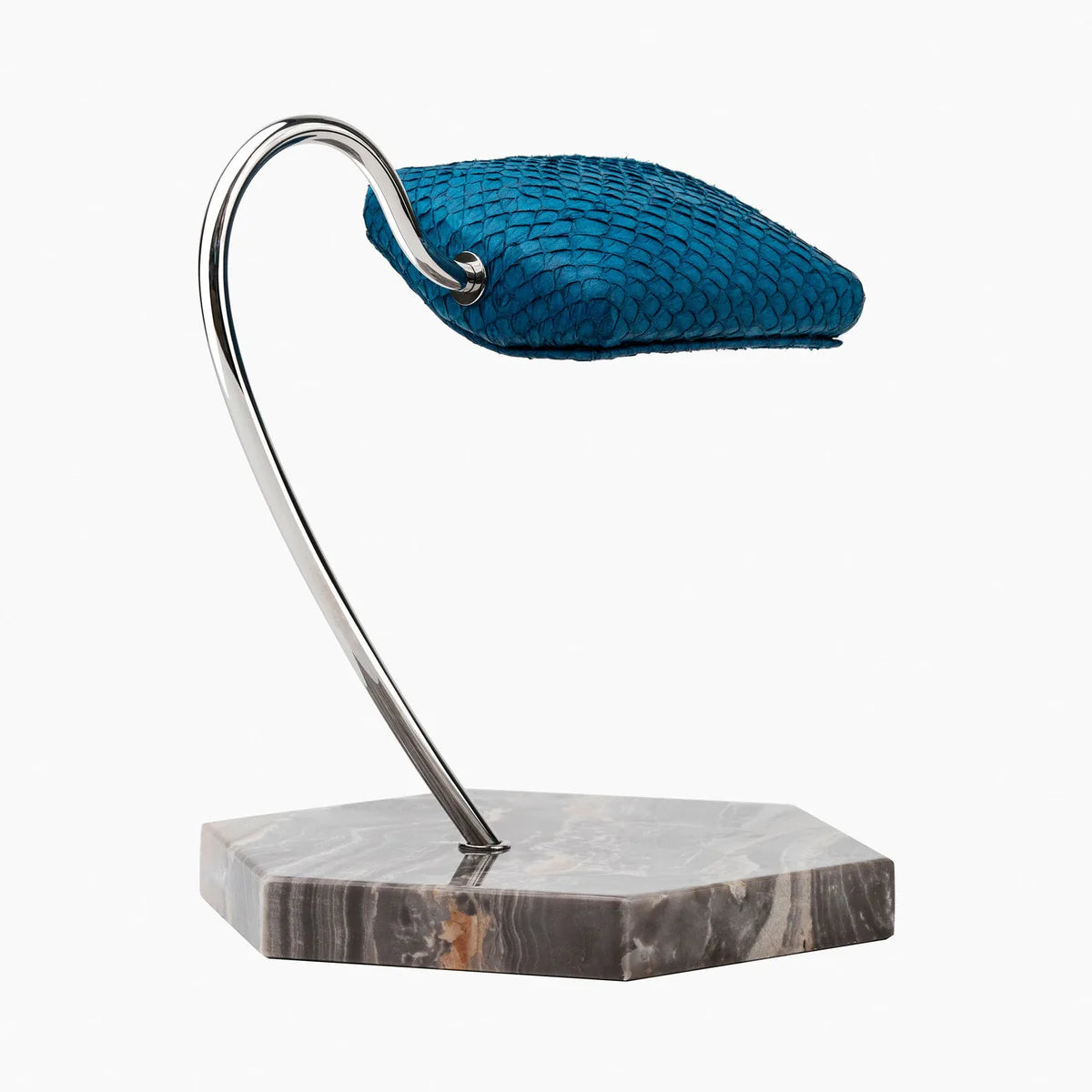 An elegant display stand featuring a blue textured cushion mounted on a sleek, curved metal support. The base of the stand is a hexagonal marble slab with shades of gray and brown veining. The design is modern and sophisticated, ideal for showcasing a wristwatch or similar item. The vibrant blue cushion contrasts beautifully with the polished metal support and marble base.