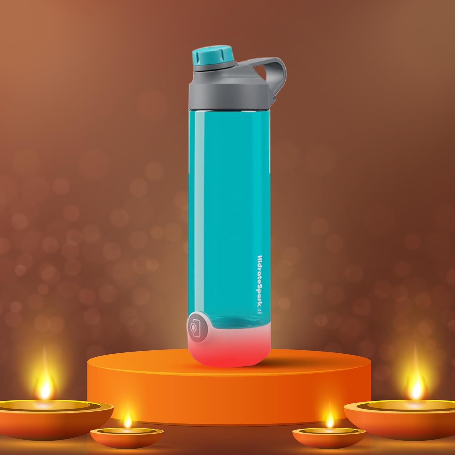 This image features the HidrateSpark smart water bottle, placed on an illuminated orange pedestal, with a warm festive background. The bottle has a gray lid with a flip-top spout and an aqua body, with its smart hydration feature highlighted by a glowing red light at the base. The background is adorned with small, glowing lamps, creating a celebratory ambiance, perfect for a festival like Diwali.