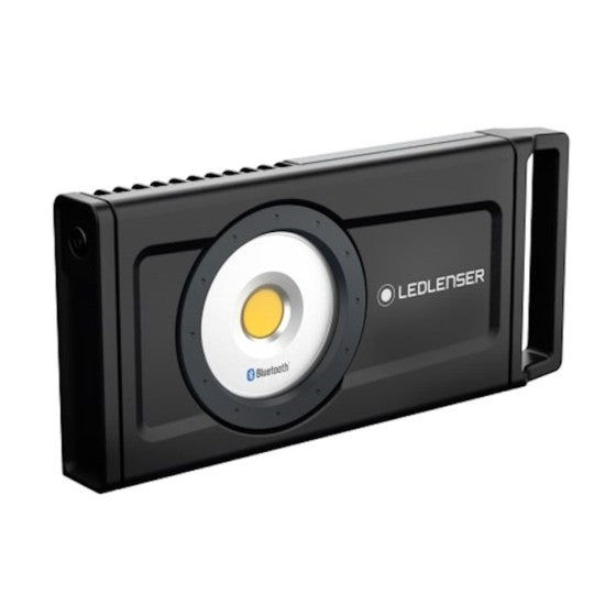  A rectangular LEDLenser portable light with a black body and a central circular LED light surrounded by a metallic ring. The light features Bluetooth functionality and has a sturdy handle on one side for easy carrying.