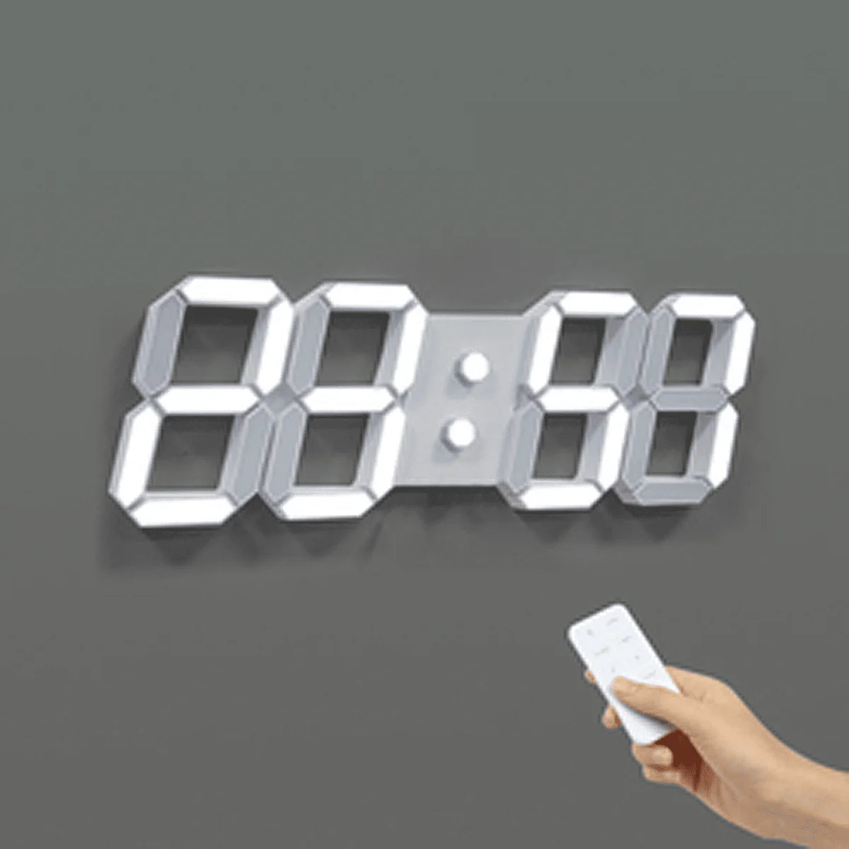 A digital wall clock with large illuminated numbers is mounted on a gray wall. The clock is displaying "88:88." A hand holding a remote control is aimed at the clock, suggesting the use of the remote to set or adjust the clock. The clock has a sleek, modern design with bright, easily readable numbers.