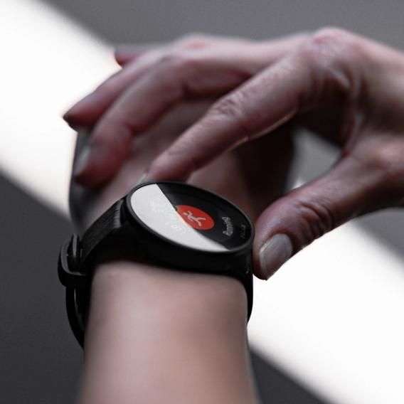 A close-up of a person interacting with a Polar Pacer smartwatch on their wrist. The smartwatch screen displays a fitness app with a red icon. The person is using their other hand to touch the watch, emphasizing the touch screen functionality