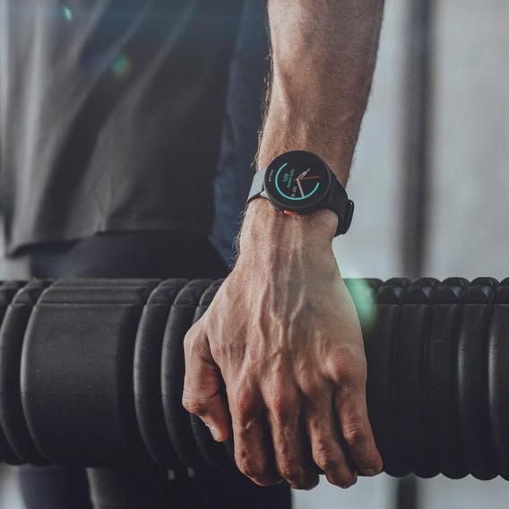  A close-up of a person's hand gripping a large black foam roller. The person is wearing a Polar Pacer smartwatch on their left wrist, which displays fitness tracking information. The person is dressed in dark athletic wear, emphasizing the sporty and functional use of the smartwatch in a fitness setting.