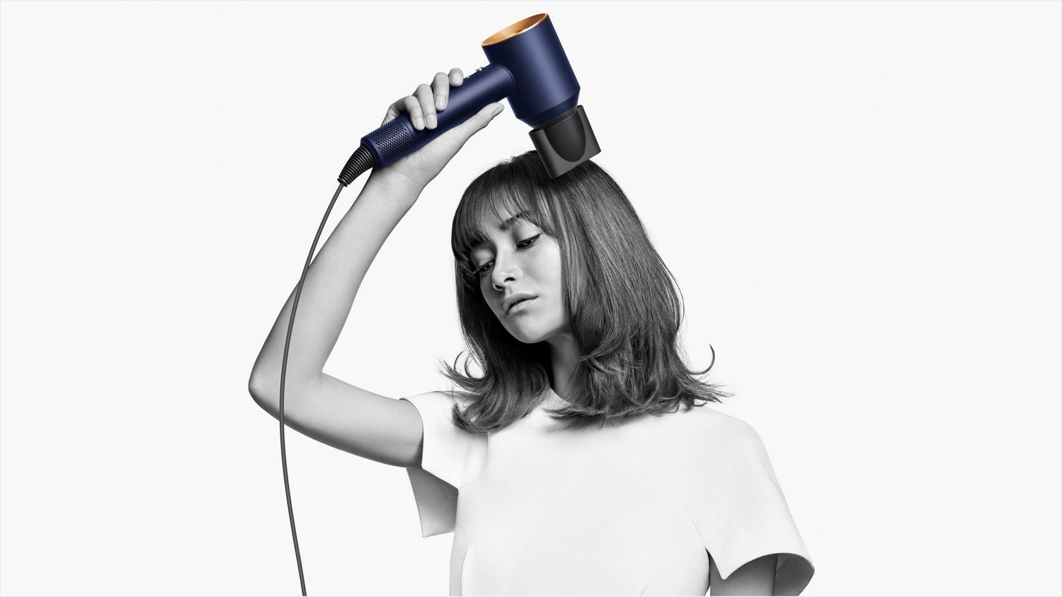 This image displays a woman using a modern navy and gold hairdryer. The minimalist background emphasizes the device's stylish design and the ease with which she uses it, reflecting a sleek and professional hair styling experience.