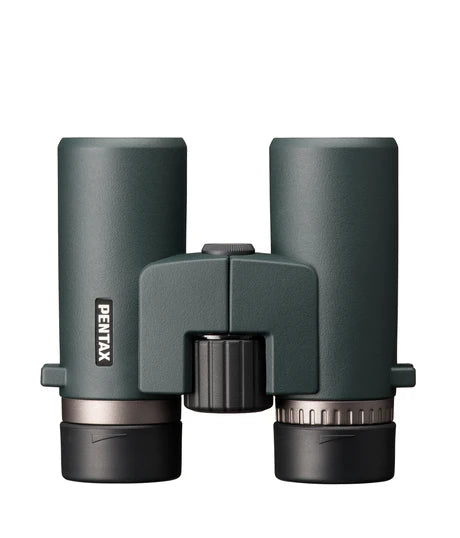 A top-down view of Ricoh Pentax AD 10x32 ED binoculars. The binoculars have a sleek, ergonomic design with a greenish matte finish. The central focusing wheel is positioned between the two barrels, with the Pentax branding visible on the left barrel. The eyepieces are capped, and the binoculars are designed for comfortable handling and ease of use, emphasizing durability and high-quality optics.