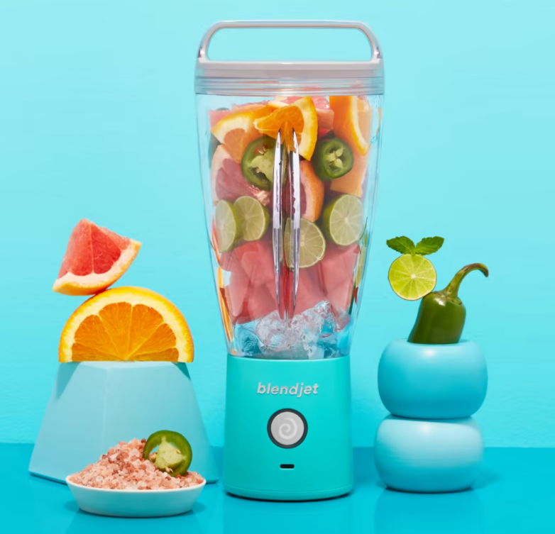 A vibrant BlendJet blender filled with colorful ingredients, including slices of grapefruit, orange, lime, jalapeño, and ice, standing on a bright turquoise background with matching decorative elements.