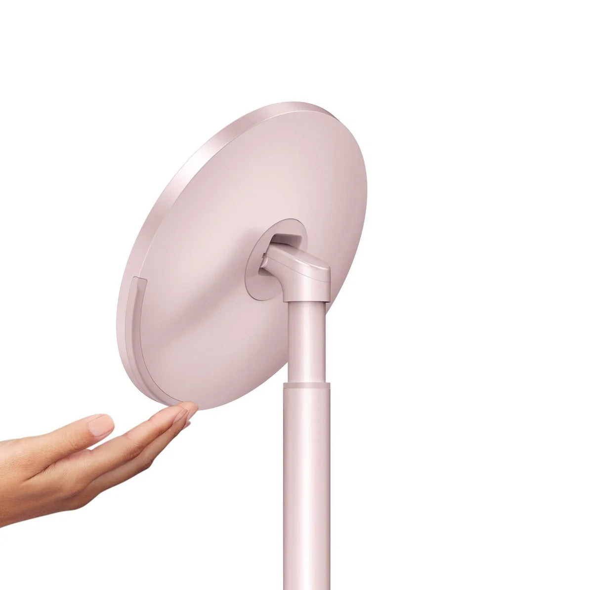 This image shows the back view of a Simplehuman makeup mirror in a soft pink finish. The focus is on the mirror's adjustable mechanism, which allows the mirror to tilt or rotate for optimal positioning. The design is sleek and minimalist, with smooth lines and a clean, uncluttered appearance.  A hand is shown interacting with the mirror, possibly demonstrating its touch-sensitive controls or the ease with which it can be adjusted. The back of the mirror is as elegantly designed as the front, ensuring that t