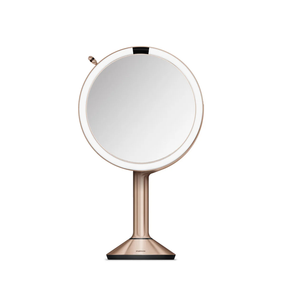 This image displays a Simplehuman makeup mirror in a rose gold finish, featuring a round, well-lit mirror with an LED light ring around the edge. The mirror is mounted on a sleek stand that tapers down to a sturdy base, ensuring stability on any surface.  The mirror's design is modern and minimalist, with a focus on both functionality and aesthetics. The LED light ring provides even illumination, which is essential for precise makeup application or grooming tasks. The overall look of the mirror suggests tha