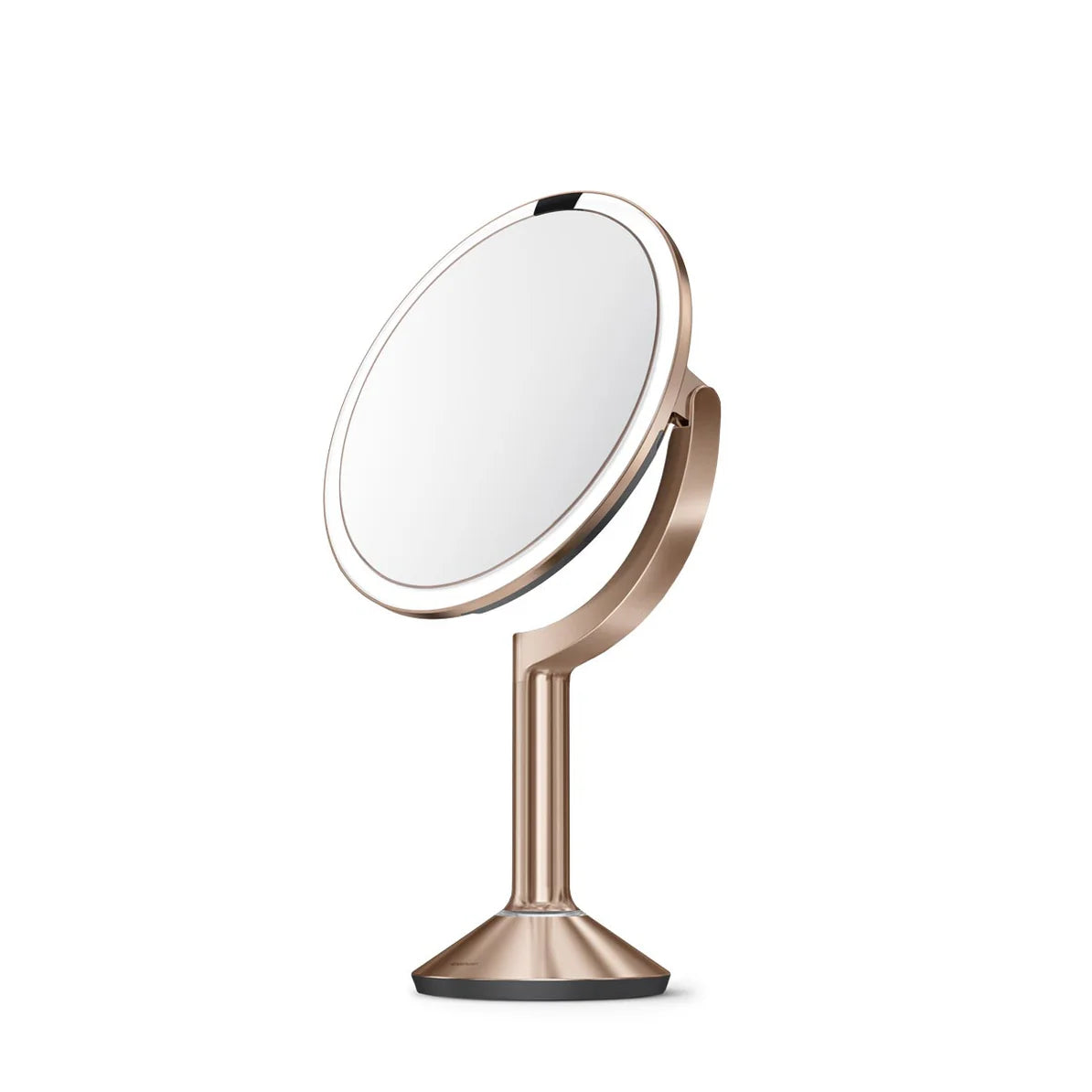 This image shows a side view of the Simplehuman makeup mirror in a rose gold finish, displaying its elegant and modern design. The mirror is slightly tilted, highlighting its adjustable angle feature, which allows for personalized positioning during use. The round mirror is surrounded by an LED light ring, providing bright, even illumination for detailed tasks such as makeup application or grooming.  The stand is sleek and tapers down to a sturdy base, ensuring stability on any surface. The rose gold color 