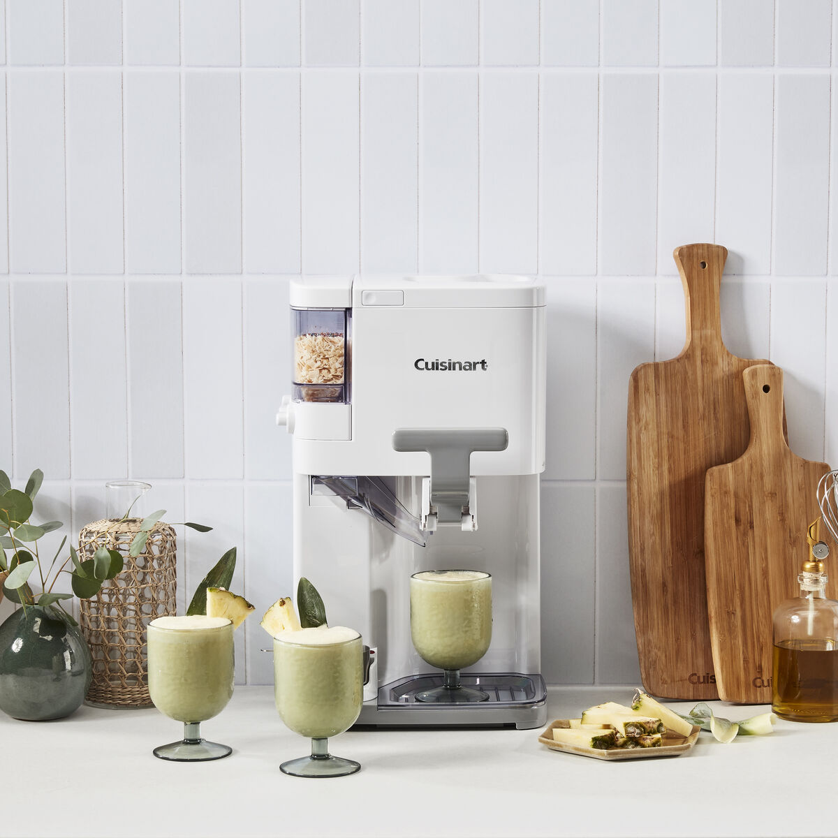 Cuisinart soft serve machine preparing matcha ice cream, with glasses of matcha soft serve and a wooden board for serving nearby.