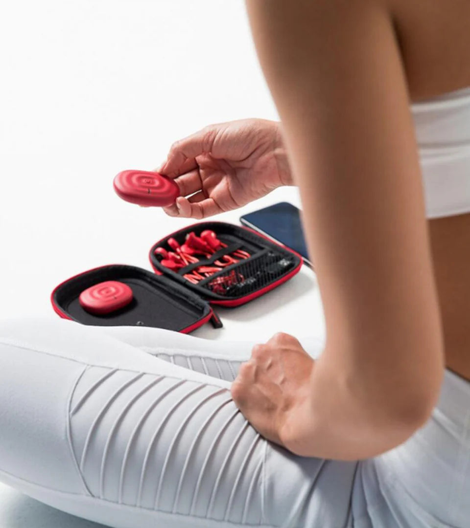 A person in activewear holding a red muscle stimulation pad with the open device kit placed nearby, highlighting the portable and user-friendly design for recovery and fitness needs.