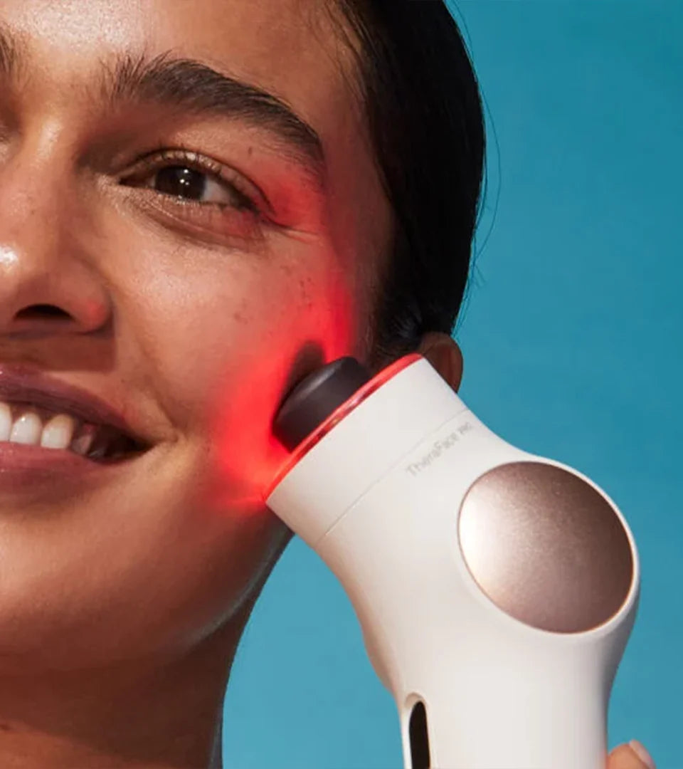 A person using a white facial therapy device emitting red light on their cheek, showcasing its advanced technology for skin rejuvenation and targeted treatment.