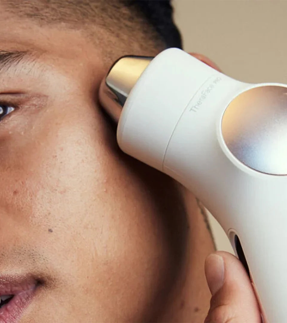 A person using a white facial therapy device with a metallic tip on their skin, demonstrating advanced skincare technology for targeted treatment and rejuvenation.