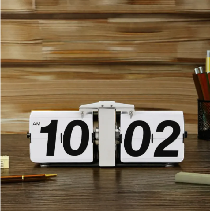 Retro flip clock displaying "10:02 AM" set on a wooden desk, surrounded by stationery items like a pen and a pencil holder, with a textured wooden background adding a classic and timeless feel to the workspace.