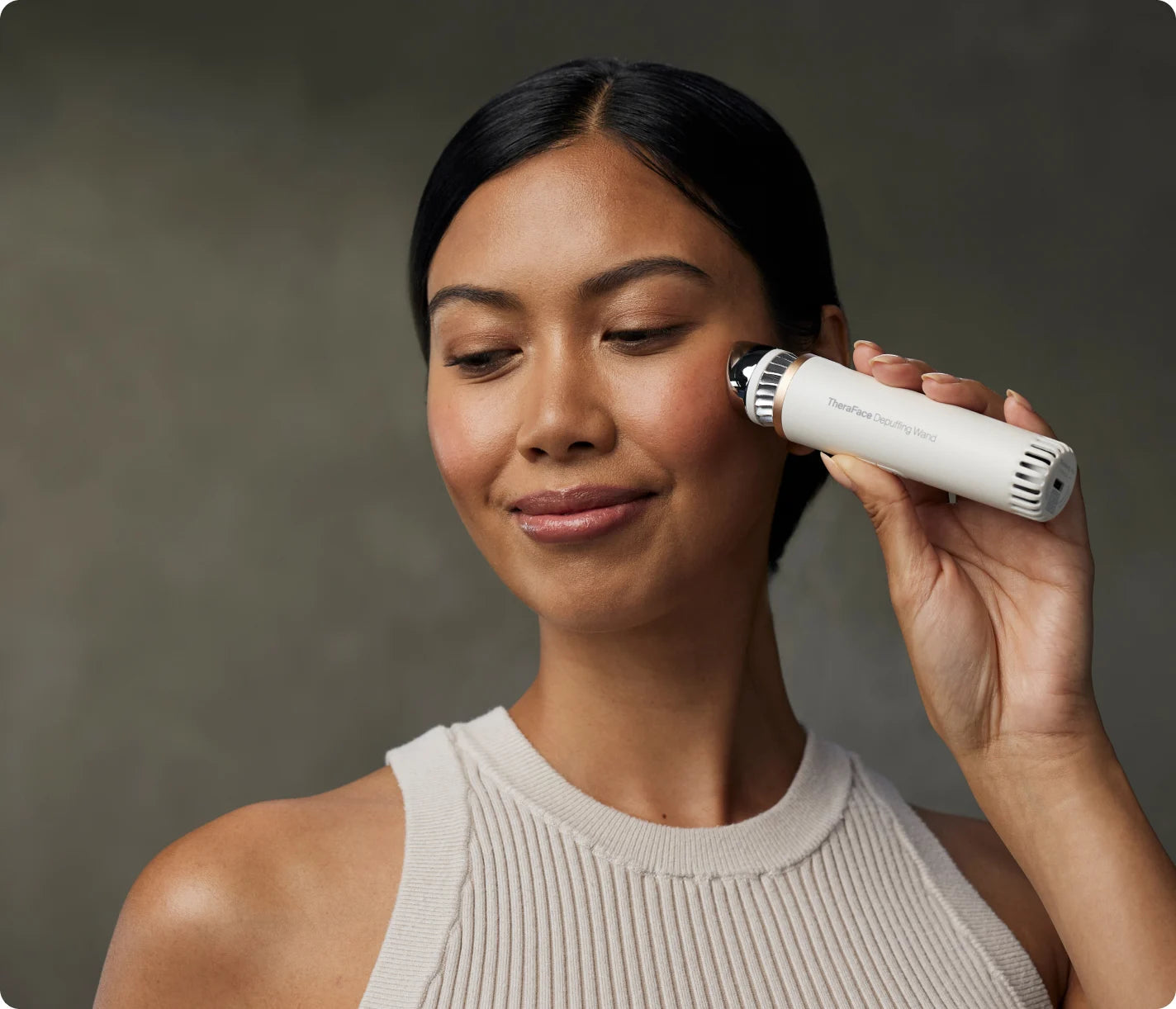Woman gliding the white TheraFace Depuffing Wand along her cheek for a cold and heat facial treatment