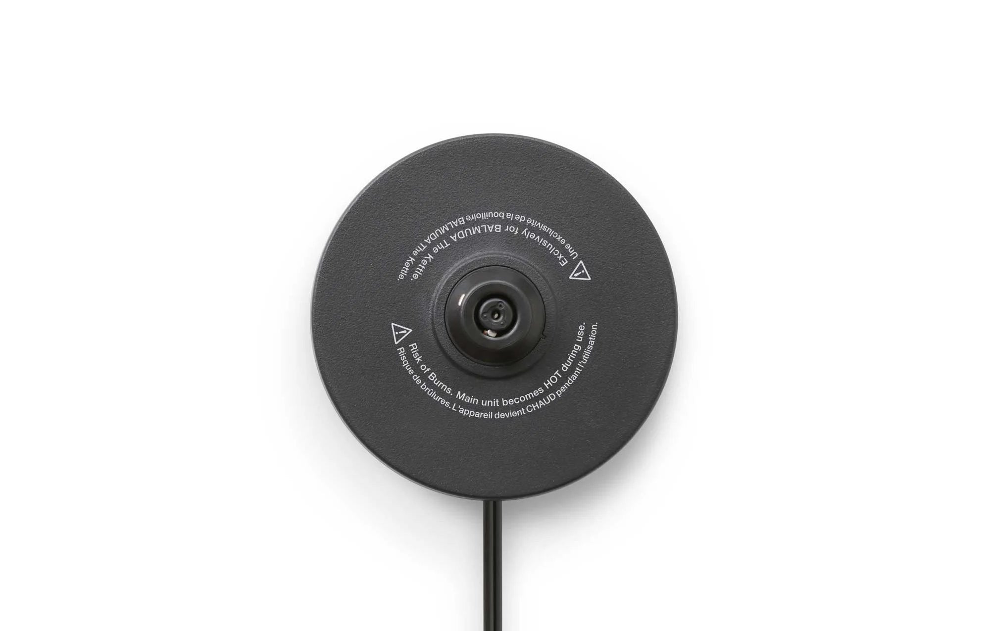  The image shows a close-up view of the underside of a circular black base, likely from an electric kettle or similar appliance. At the center is a black connector or plug, surrounded by printed safety warnings and usage instructions in a circular pattern.