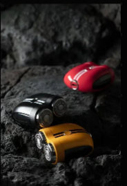 This image features the "Sports Car Shaver" models in three distinct colors: red, black, and yellow, displayed against a rugged, rocky backdrop. The shavers are positioned to emphasize their sleek, aerodynamic designs, reminiscent of sports cars, with metallic accents that add to their premium appearance.  The choice of a rugged setting contrasts with the polished look of the shavers, possibly symbolizing their durability and performance, much like high-end sports cars that are built to handle both the fast