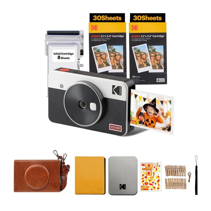 An image displaying a **Kodak C210R instant camera bundle**, which includes the camera, photo cartridges, an initial cartridge pack, a leather carrying case, photo albums, decorative clips, and accessories for capturing and displaying instant memories.