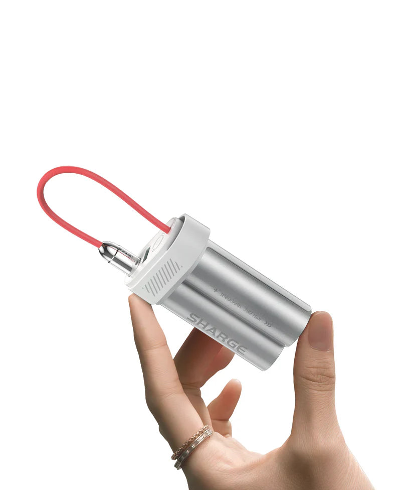 A person holding the SHARGE portable power bank between their fingers, showcasing its lightweight and compact dual-cylinder metallic design with a red flexible charging cable. The sleek and stylish design highlights its portability for on-the-go charging needs.