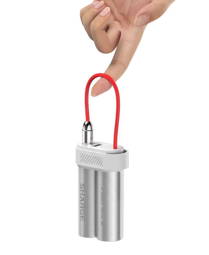 A compact SHARGE portable power bank with a metallic silver dual-cylinder design and a red flexible charging cable, shown being effortlessly lifted by a person's finger to emphasize its lightweight and portable design.