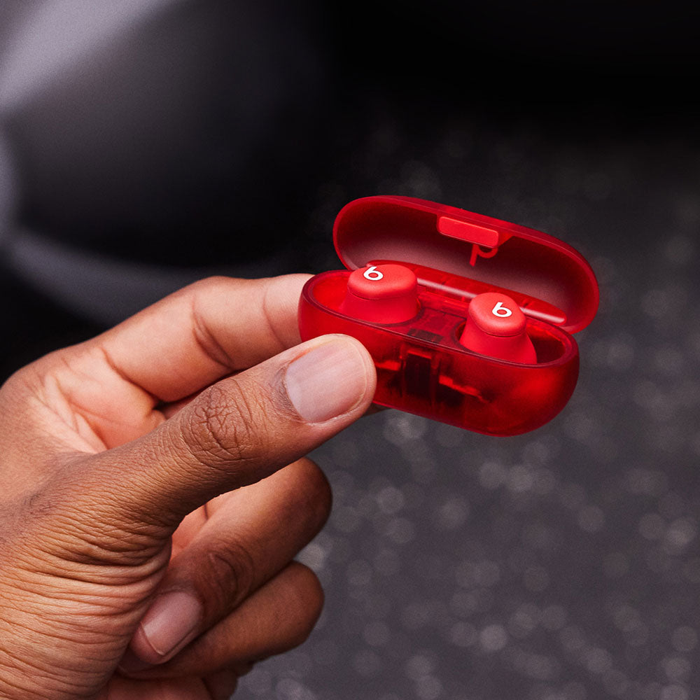 Hand holding red Beats wireless earbuds in a compact charging case, showcasing portability and sleek design.