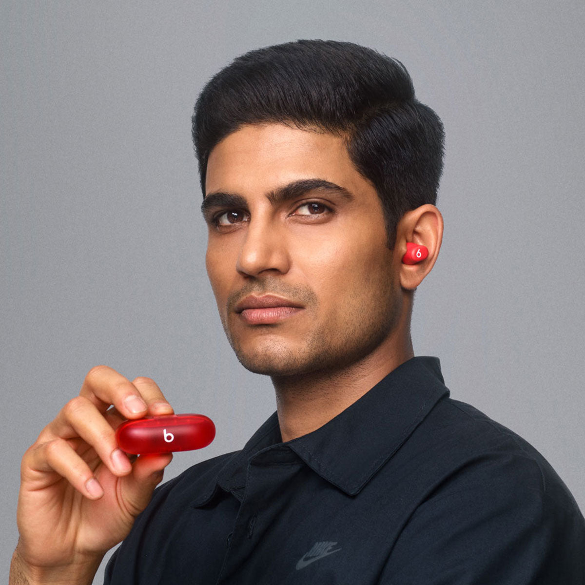 Man wearing red Beats wireless earbuds while holding the matching charging case, highlighting the compact and stylish design.